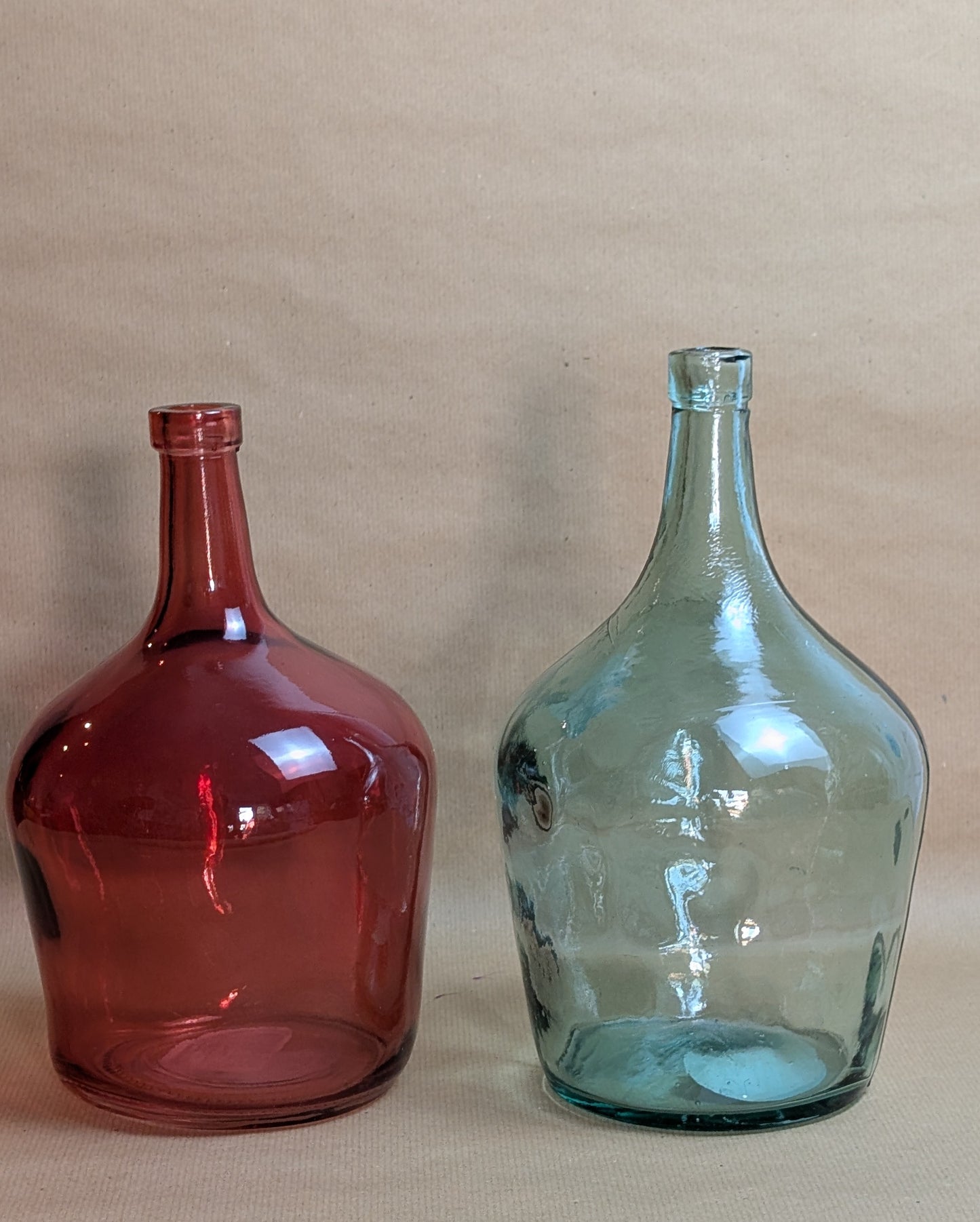 Two glass bottles, one red and one green, on a beige background