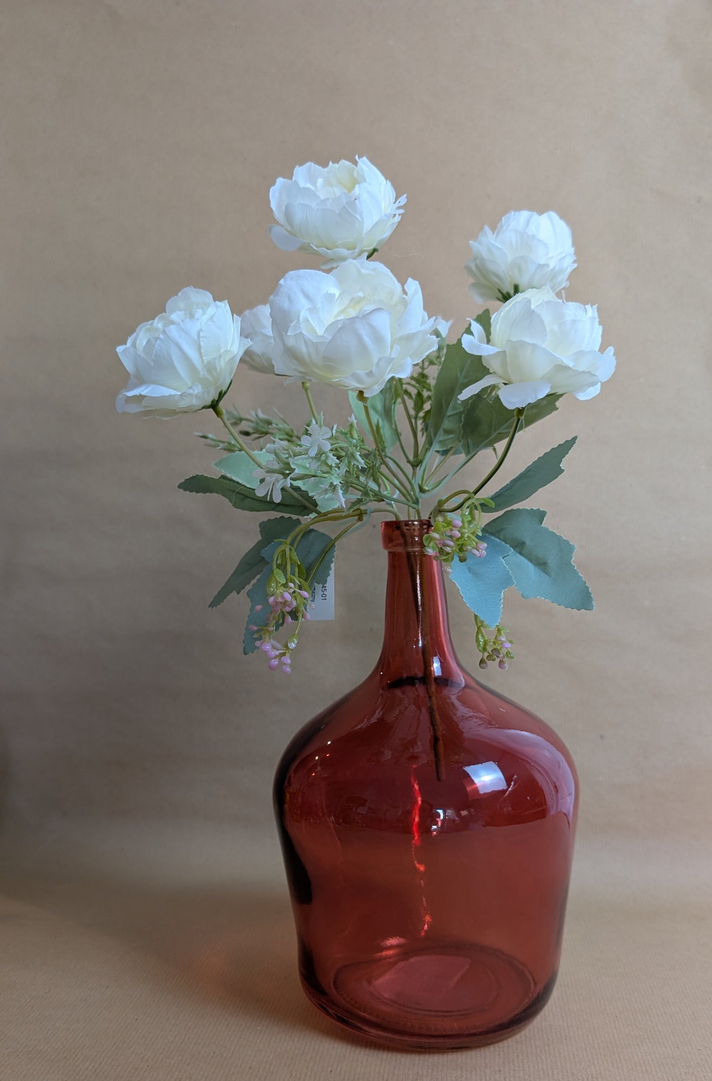 Red glass bottle with white flowers on a beige background