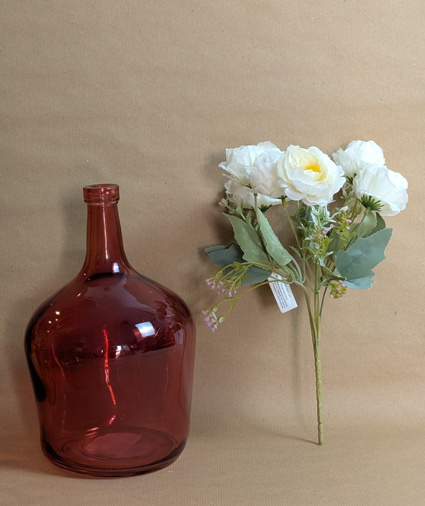 Red glass bottle and bouquet of white flowers on a beige background