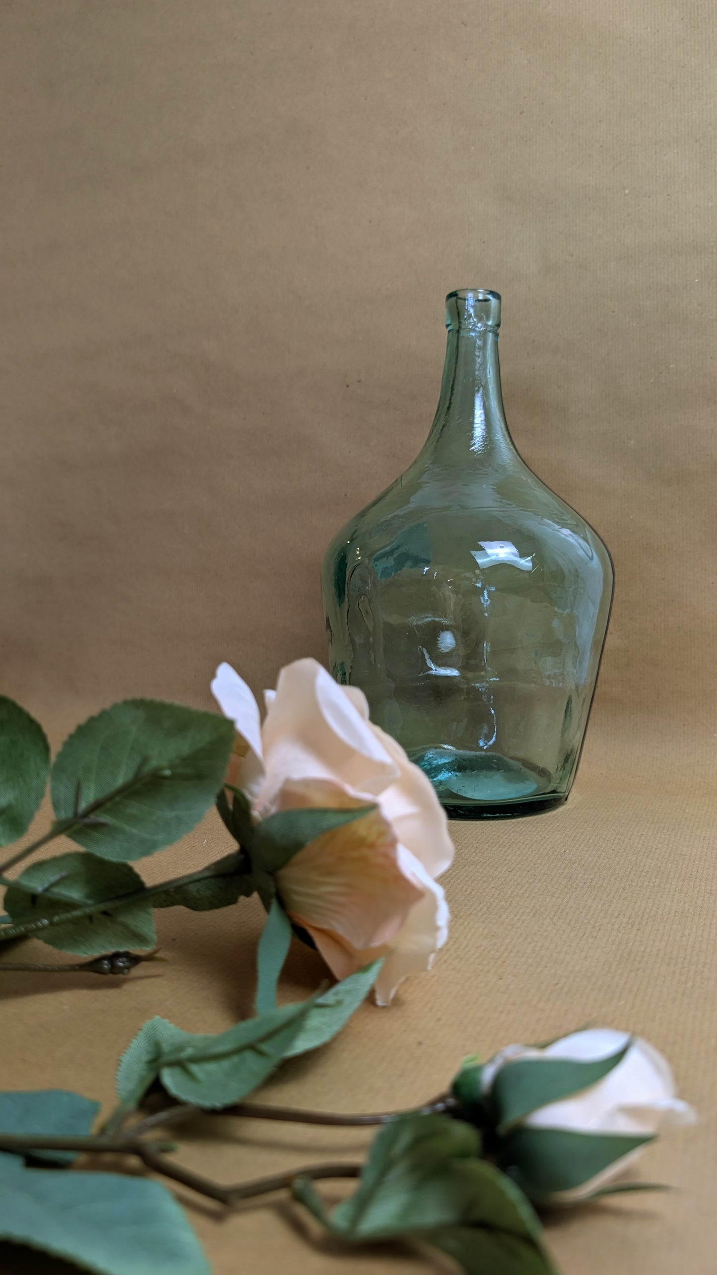 Green glass bottle with a white flower on a beige background