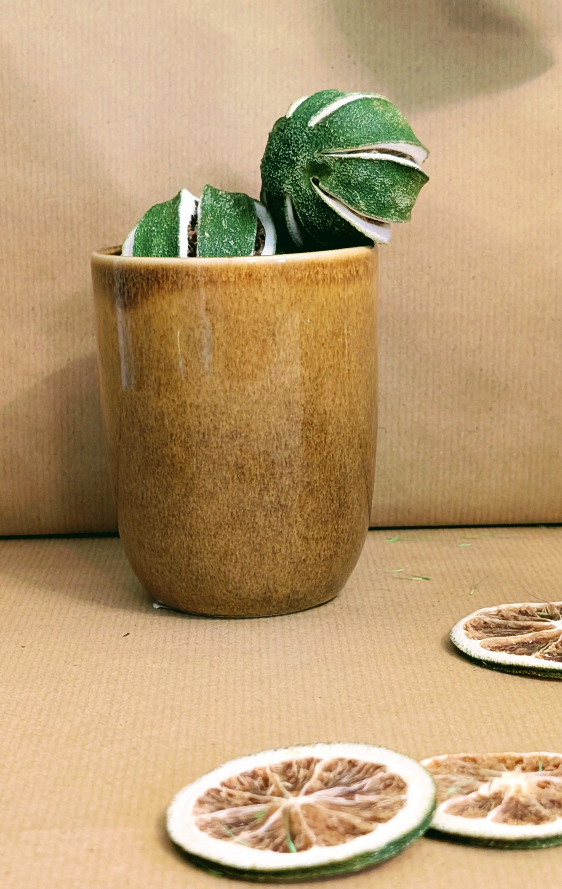 Decorative green and white spherical objects in a brown pot on a beige surface with dried orange slices.