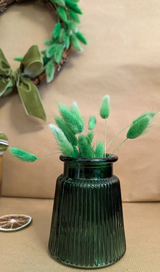 Green vase with decorative greenery on a beige surface