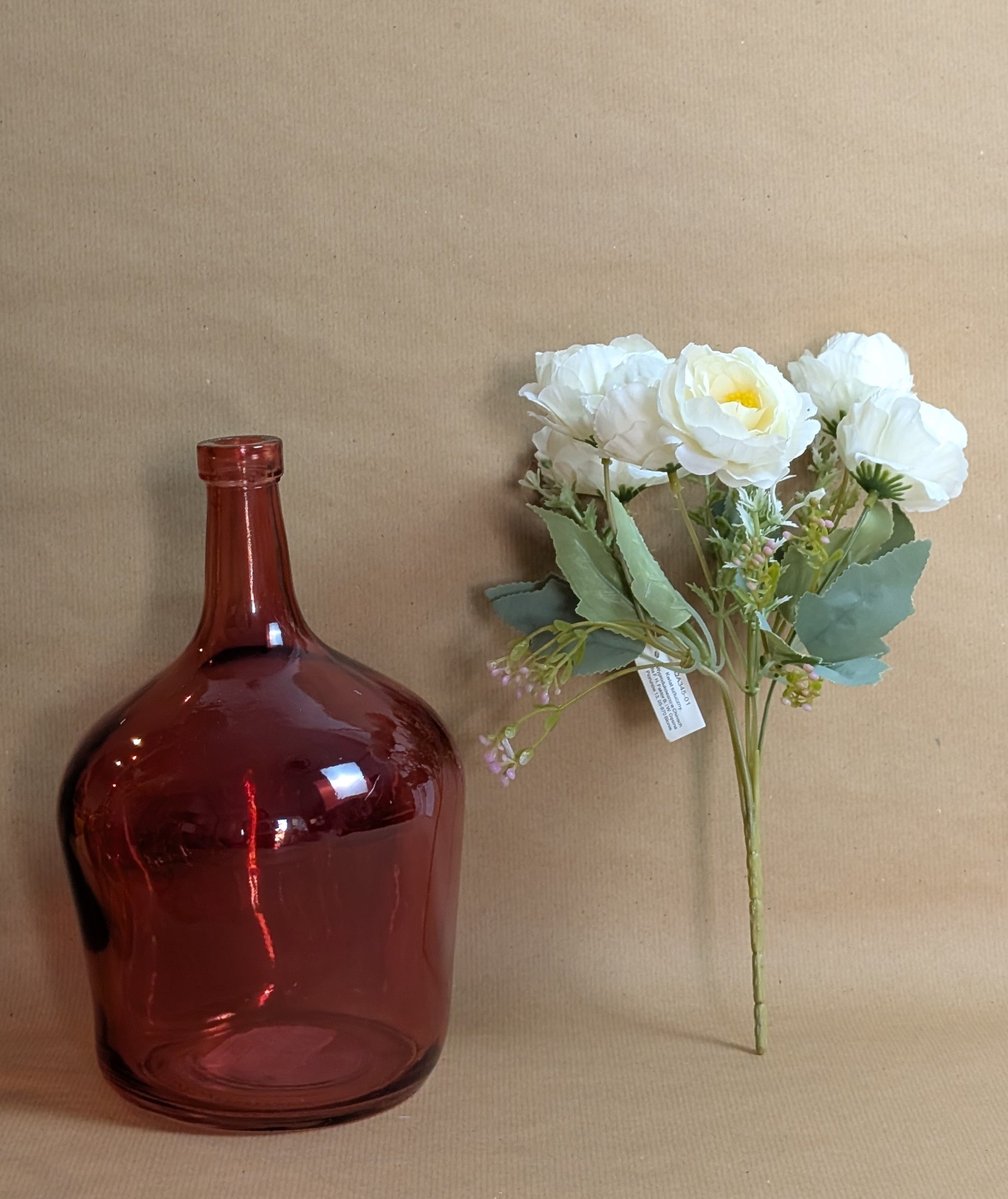 Red glass bottle and bouquet of white flowers on a beige background