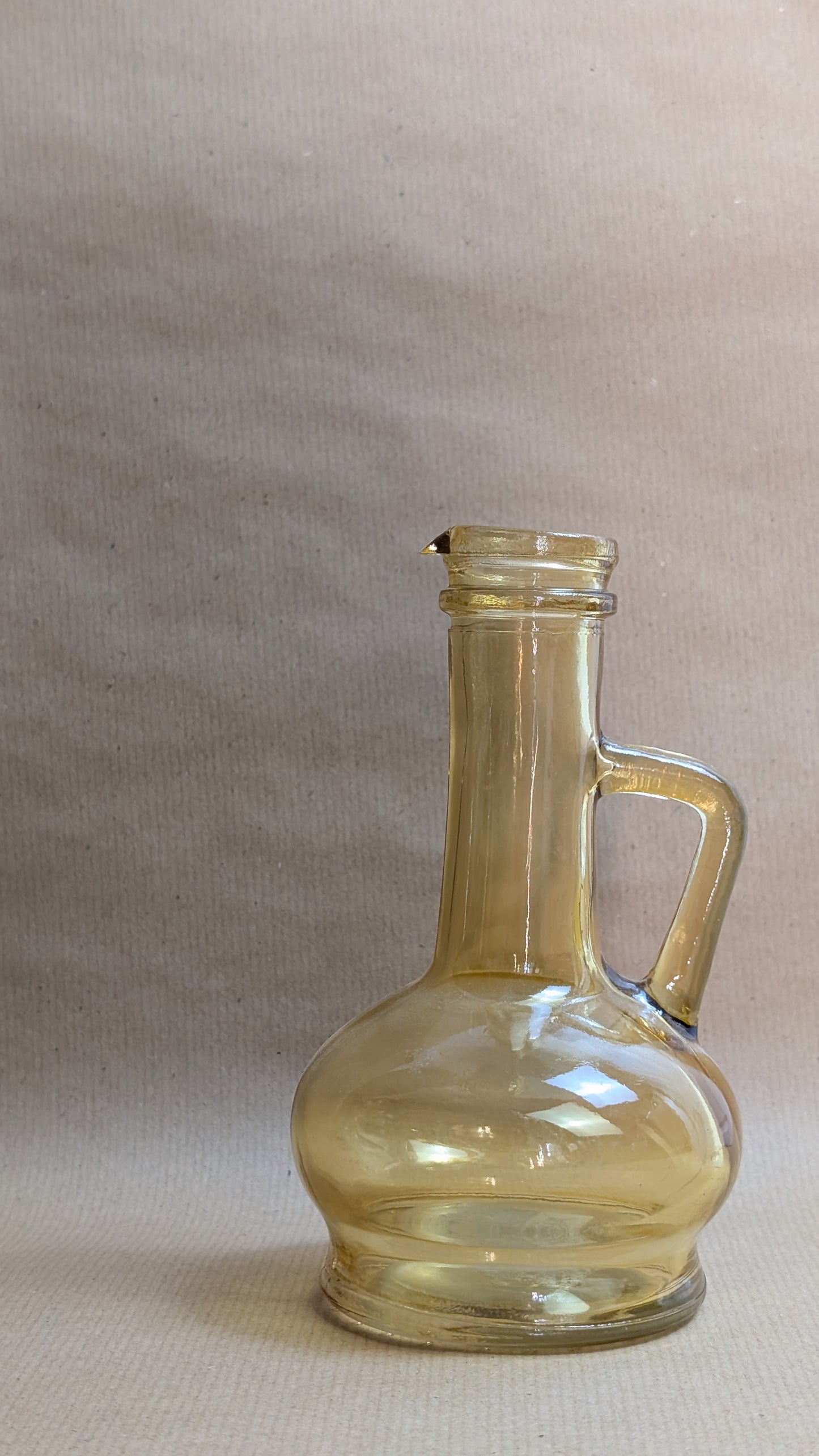 Clear glass bottle with handle on a beige background