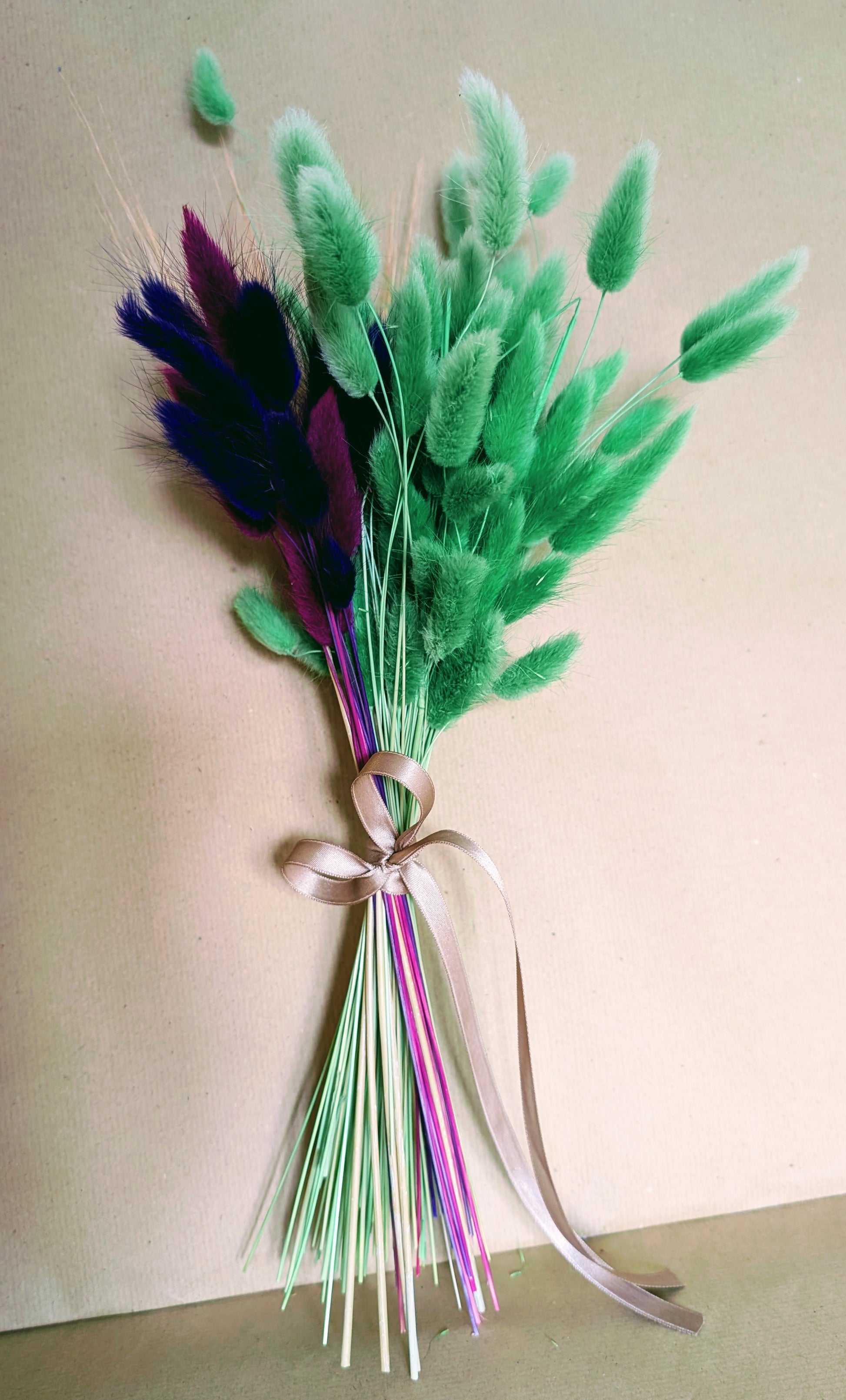 Bouquet of green and purple feathers tied with a ribbon on a light background