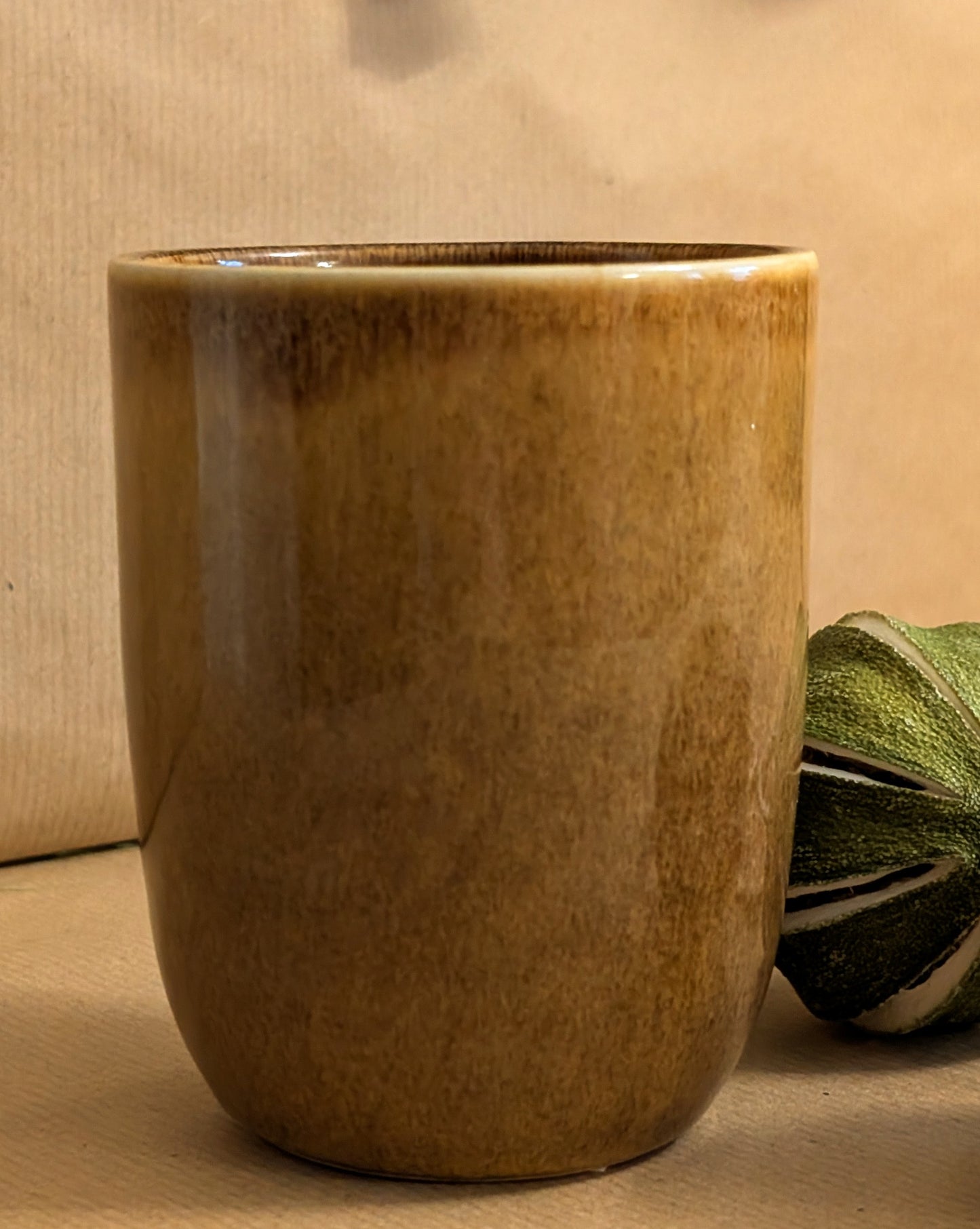 Brown ceramic cup on a beige surface with a green leafy vegetable.