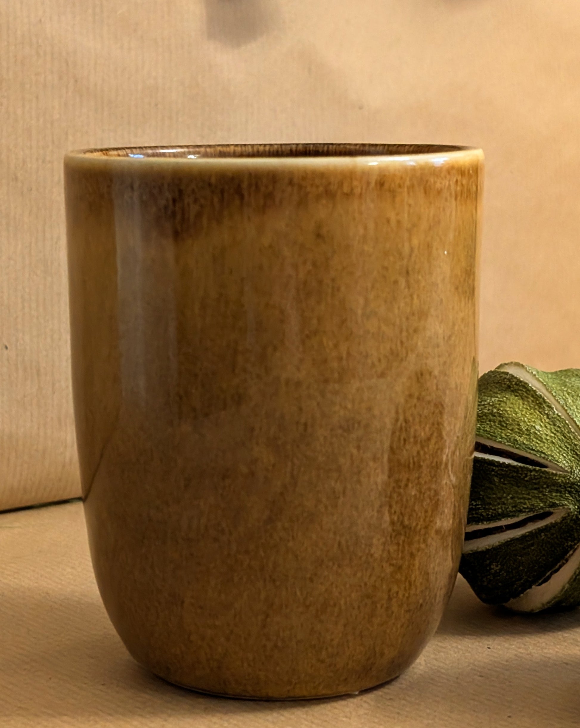 Brown ceramic cup on a beige surface with a green leafy vegetable.